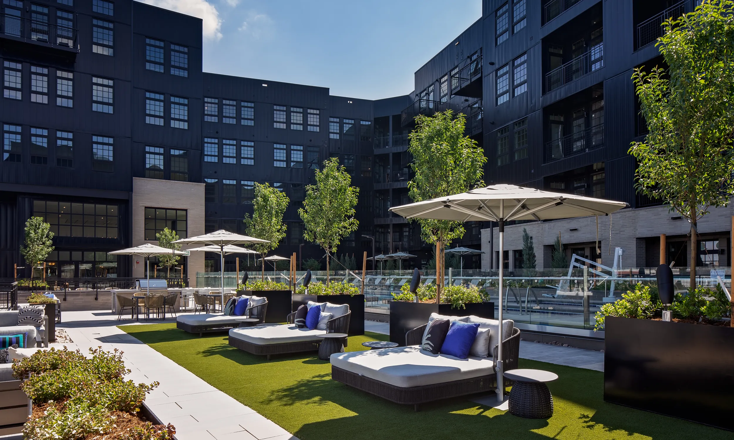 Chic urban apartment complex featuring a stylish outdoor terrace with modern seating, lush greenery, and large umbrellas, perfect for relaxation and gatherings modera art park denver co