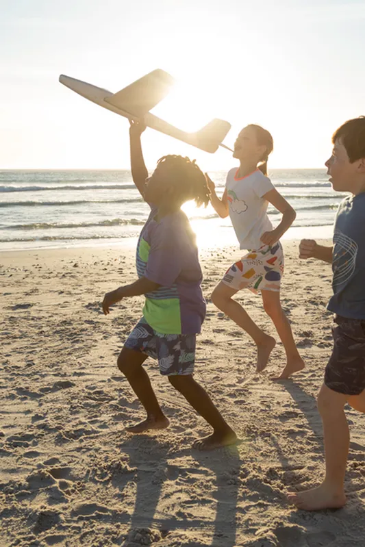 Joyful children playing with a toy airplane on a sunny beach, capturing the essence of carefree fun and adventure by the sea.