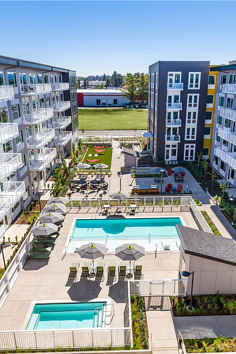 Luxurious apartment complex featuring modern architecture, spacious balconies, and a stunning central pool area with sun loungers and umbrellas.