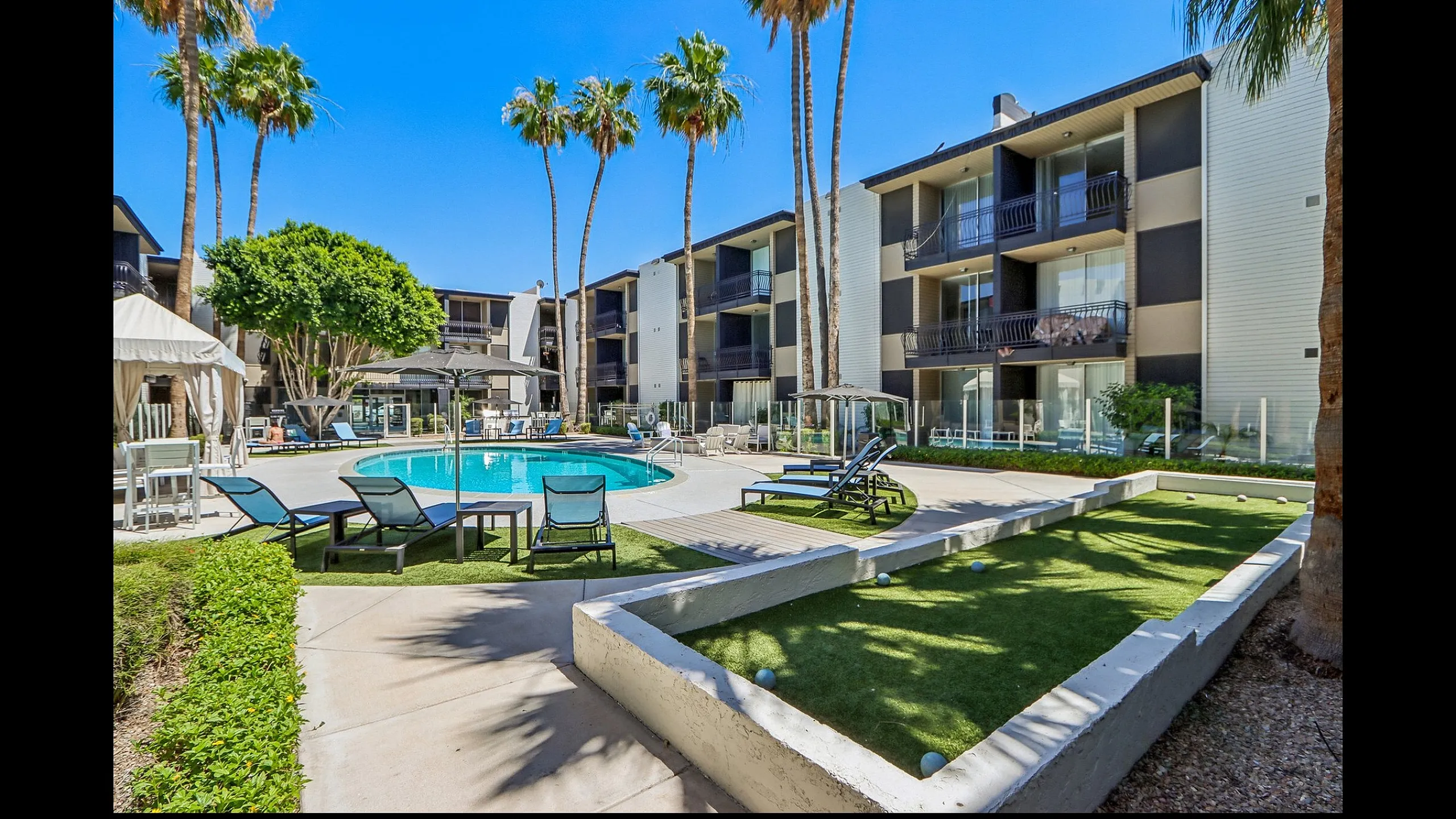 Beautiful apartment complex featuring a sparkling pool, sun loungers, and lush palm trees, offering a resort-style living experience.