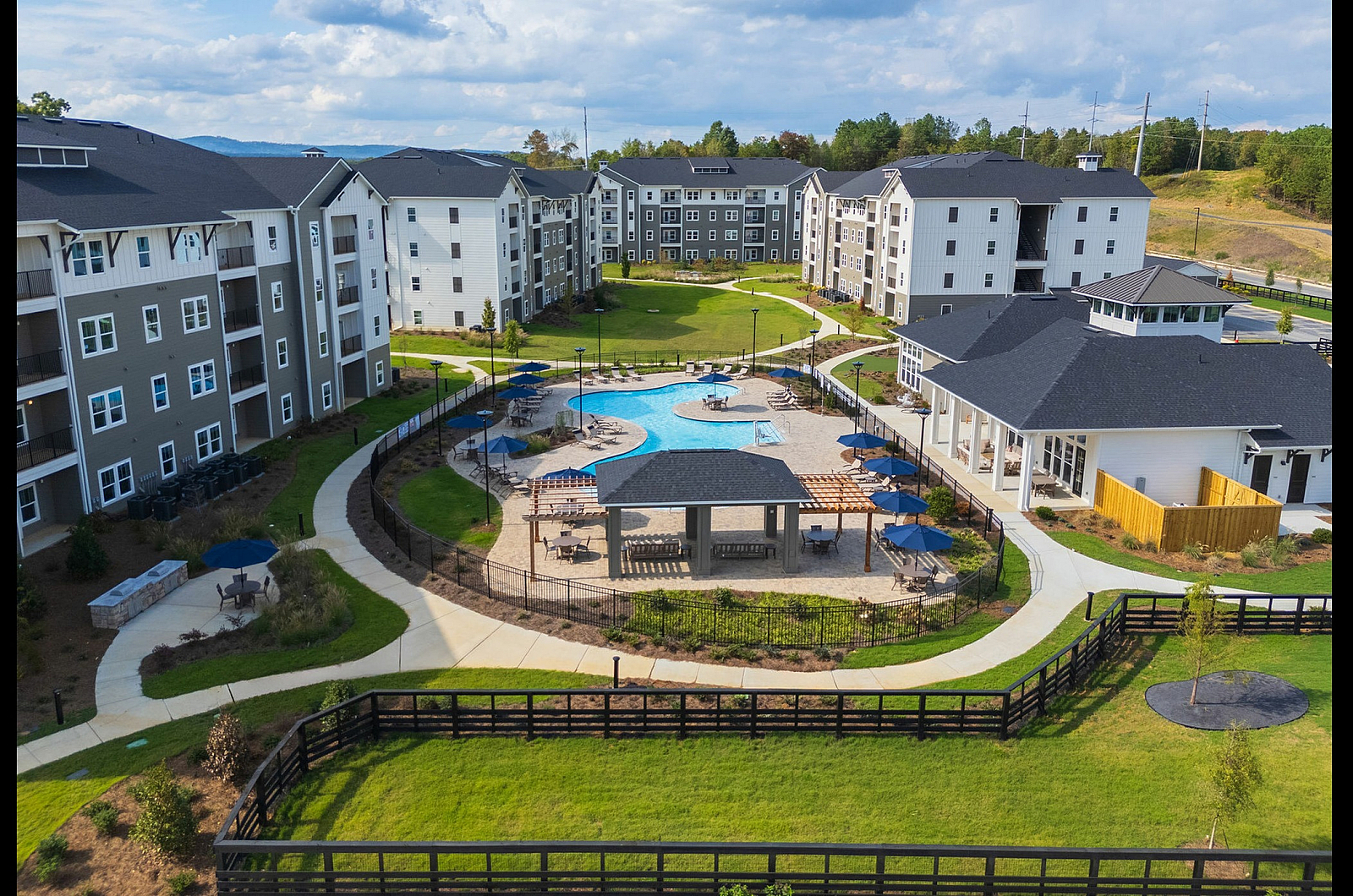 Aerial view of a modern apartment complex featuring lush landscaping, a large swimming pool, and spacious outdoor amenities.