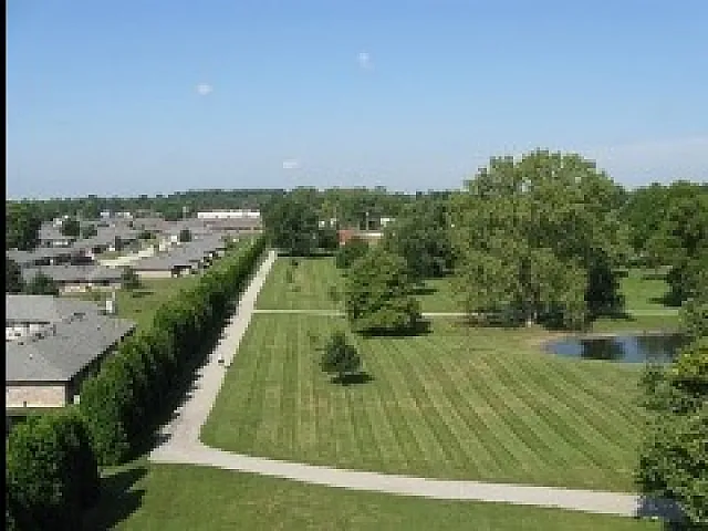 Beautiful aerial view of a green neighborhood park with manicured lawns, tree-lined paths, and a serene pond, perfect for outdoor relaxation.