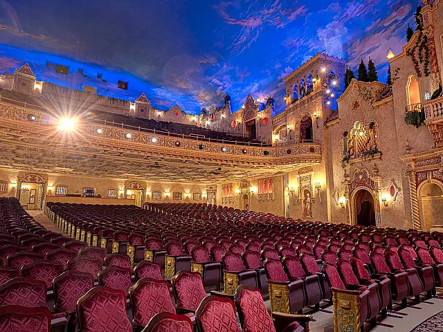Ornate theater interior with luxurious red seating, detailed architecture, and a sky-painted ceiling creating an enchanting atmosphere.