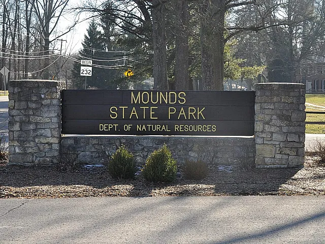 Inviting stone entrance sign to Mounds State Park, surrounded by serene natural beauty and open green spaces.