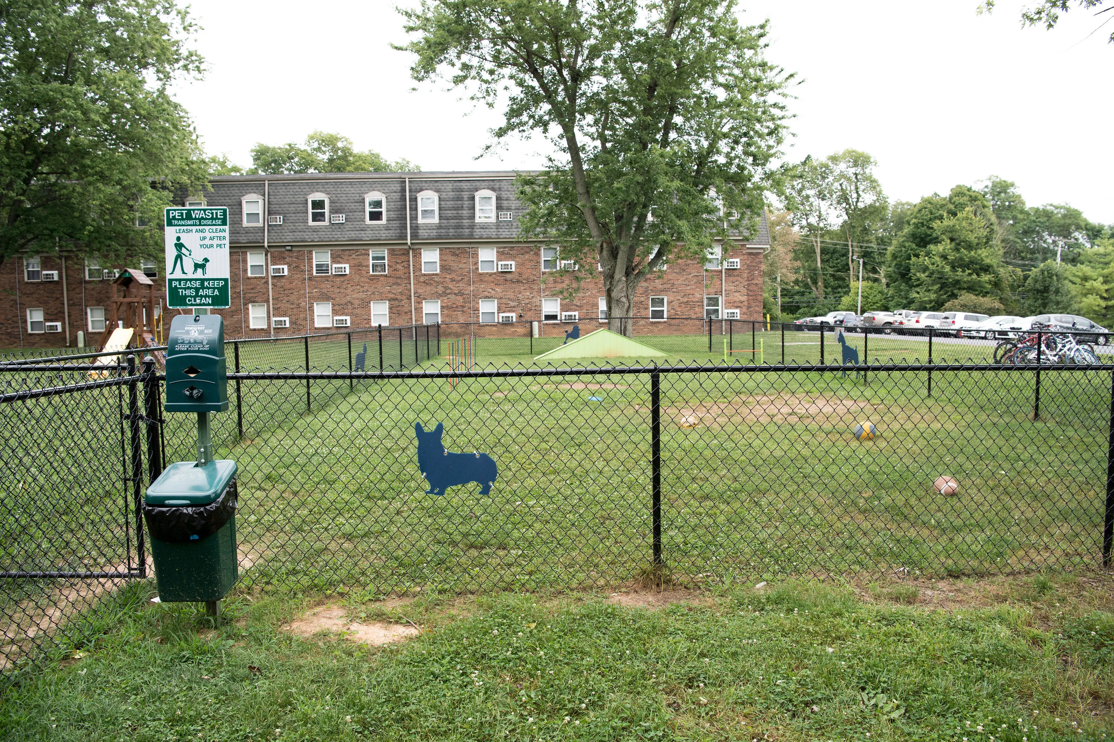 Charming dog-friendly apartment complex with a spacious fenced play area, surrounded by lush greenery and ample parking.