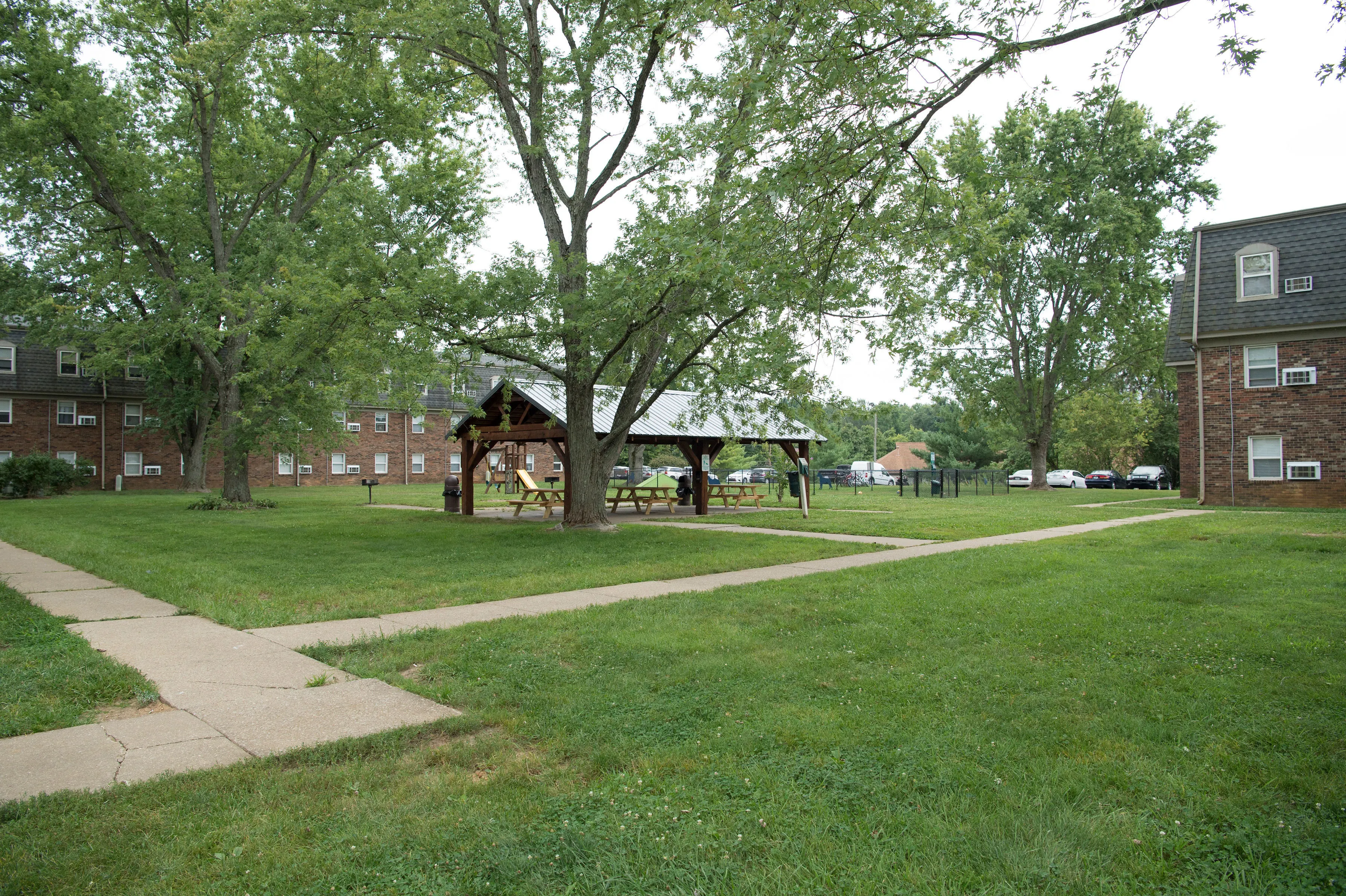 Charming apartment complex with lush green lawns, featuring a scenic courtyard with a picnic pavilion and mature trees.