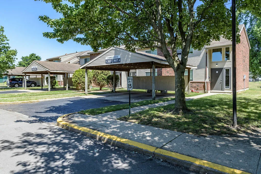 Charming apartment building with a covered parking area, surrounded by lush green trees and well-maintained lawns.