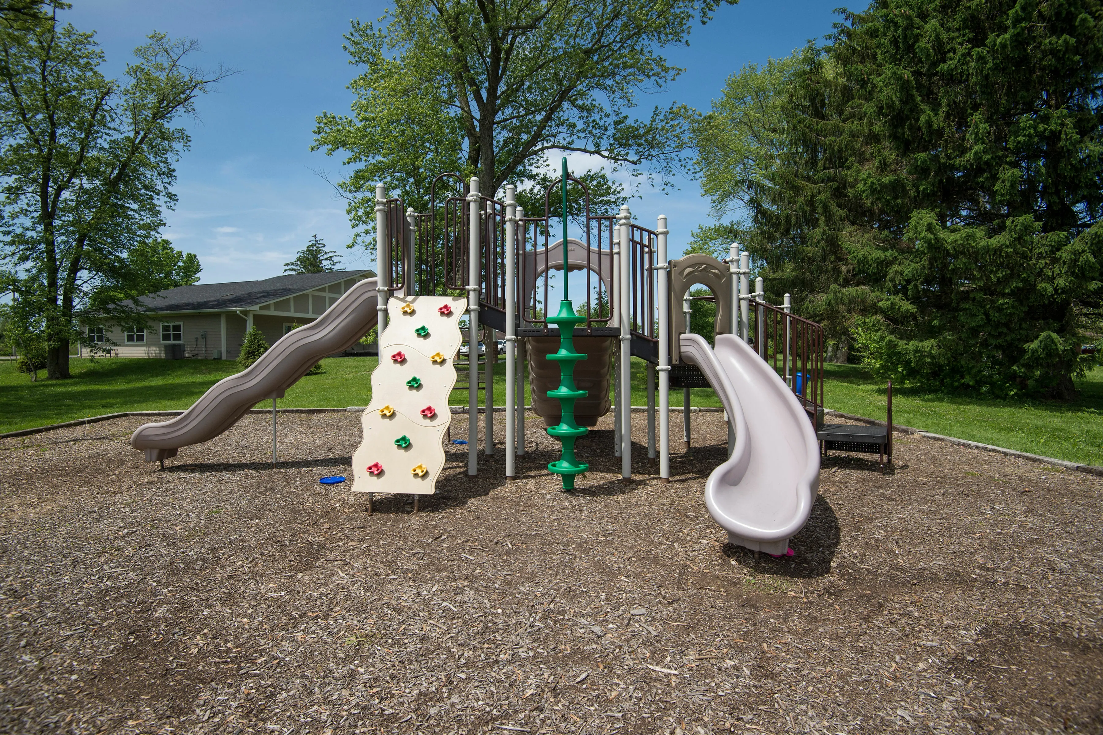 Vibrant outdoor playground with slides, climbing wall, and lush green surroundings.