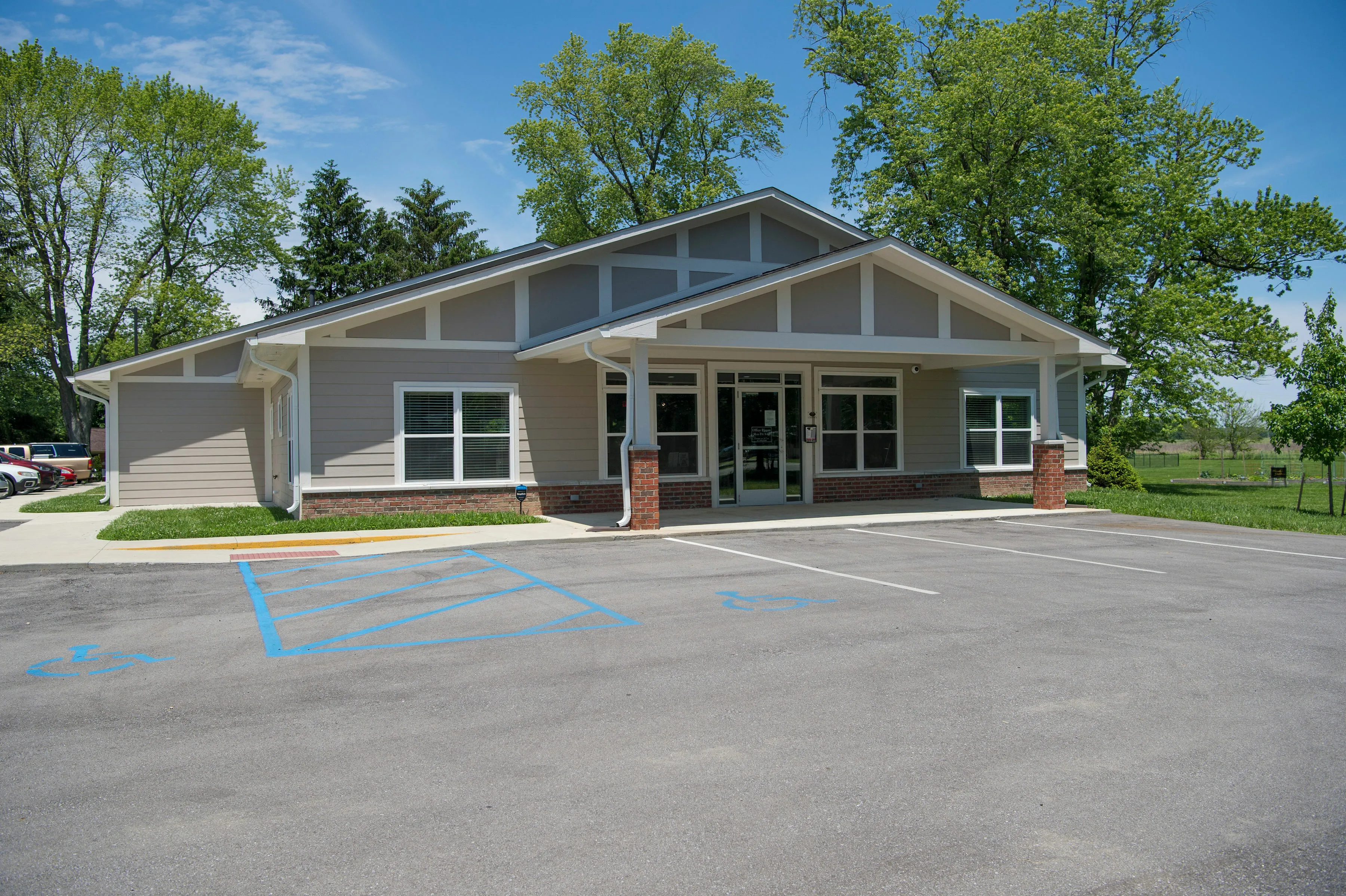 Charming modern single-story building with large windows, ample parking, and lush green surroundings under a clear blue sky.