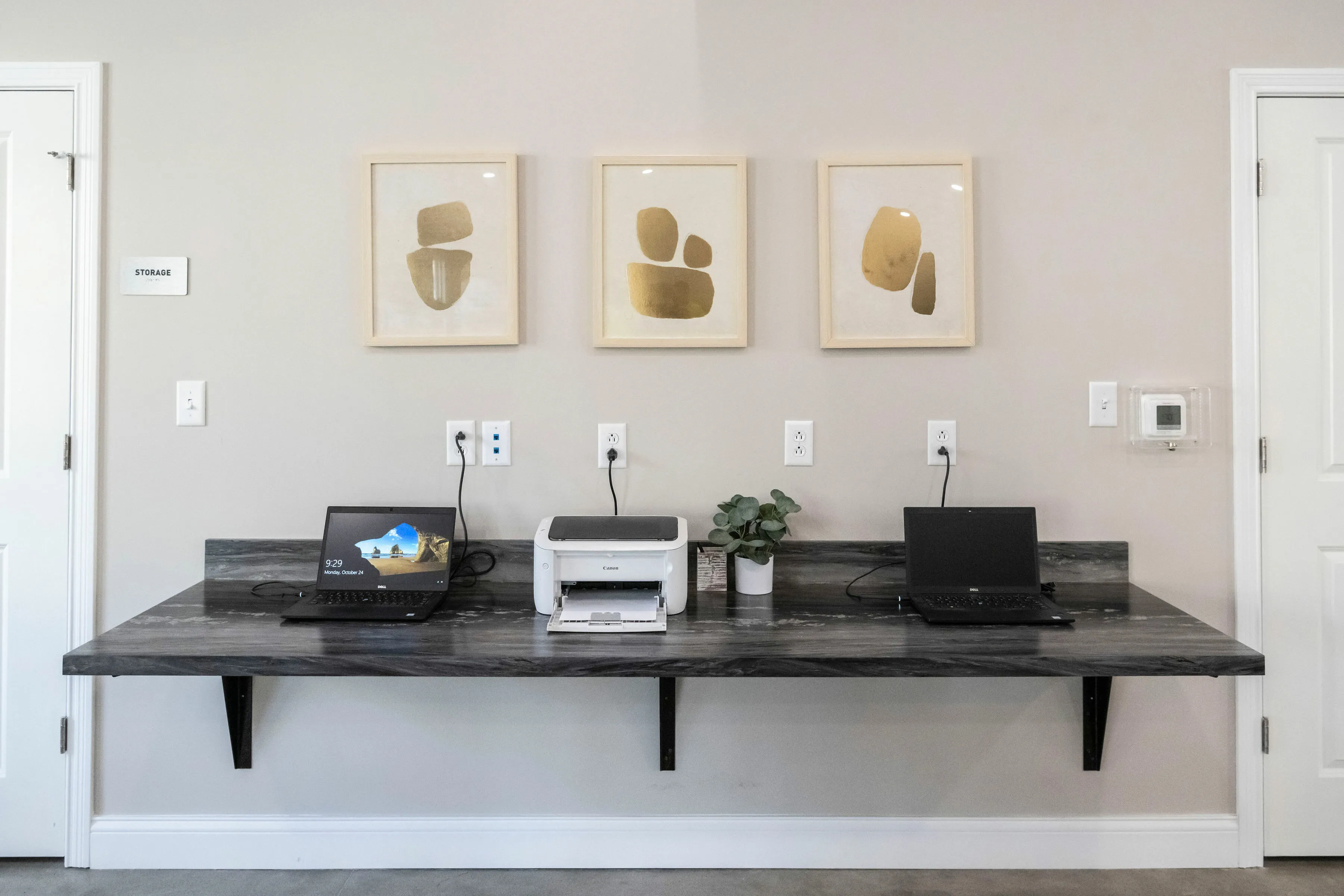 Modern home office setup with sleek laptops, a printer, and abstract art on the wall, creating a perfect workspace.