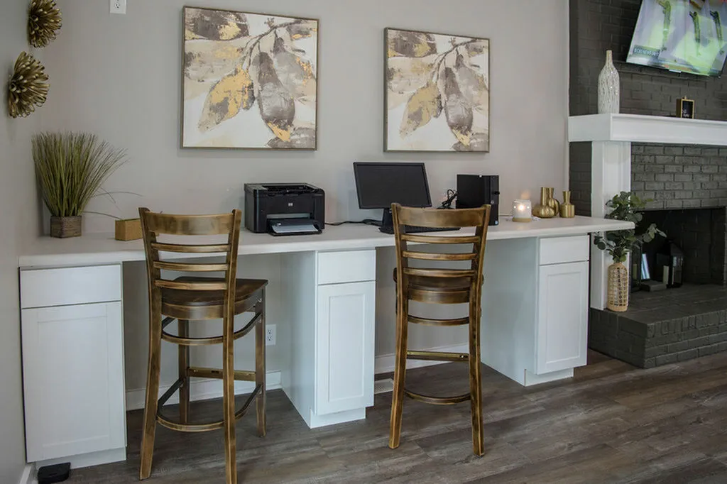 Elegant home office setup with stylish wooden chairs, dual workstations, and contemporary art, next to a cozy brick fireplace.