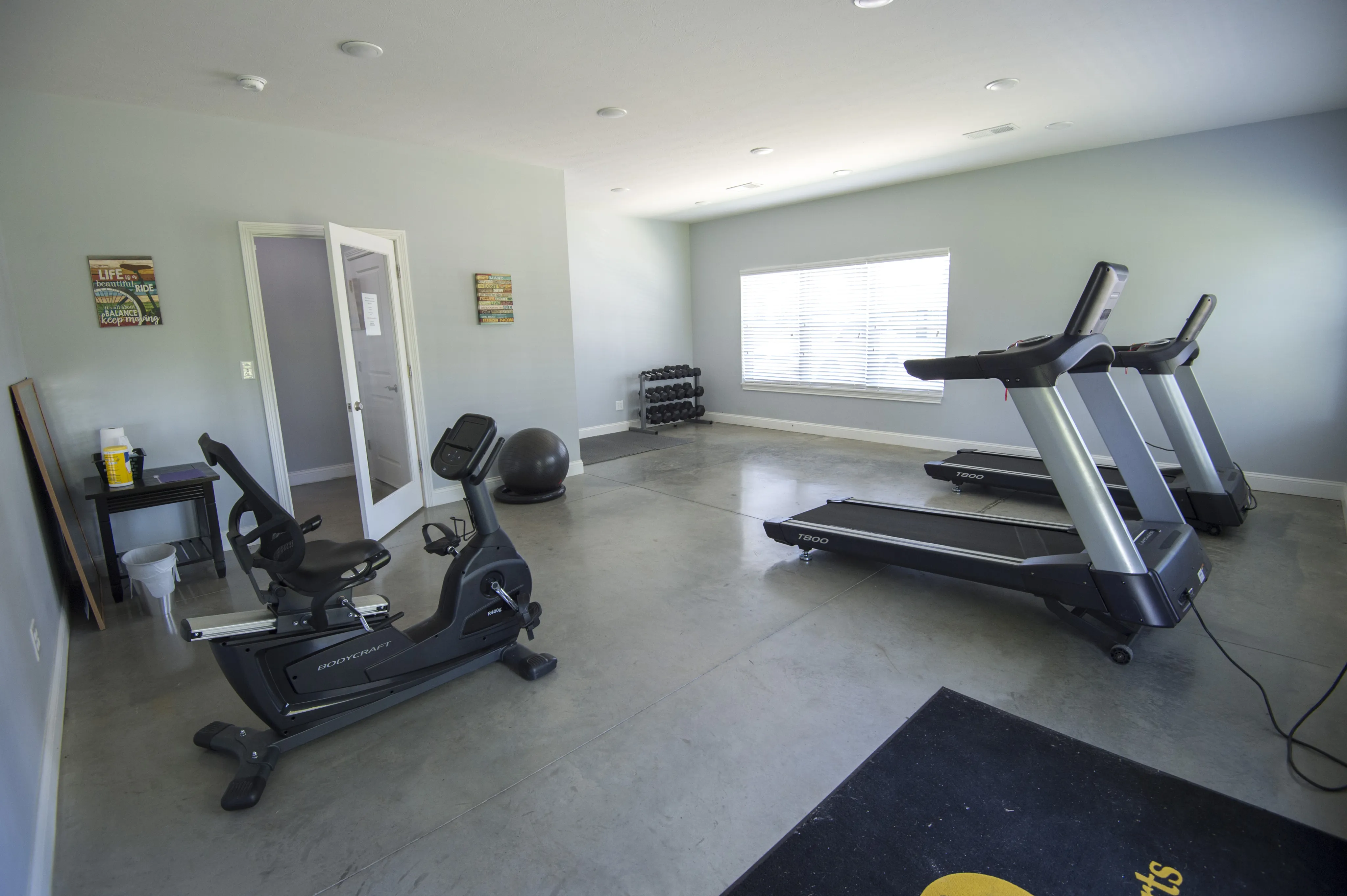 Modern fitness room featuring state-of-the-art treadmills, stationary bike, and free weights in a bright, inviting space.
