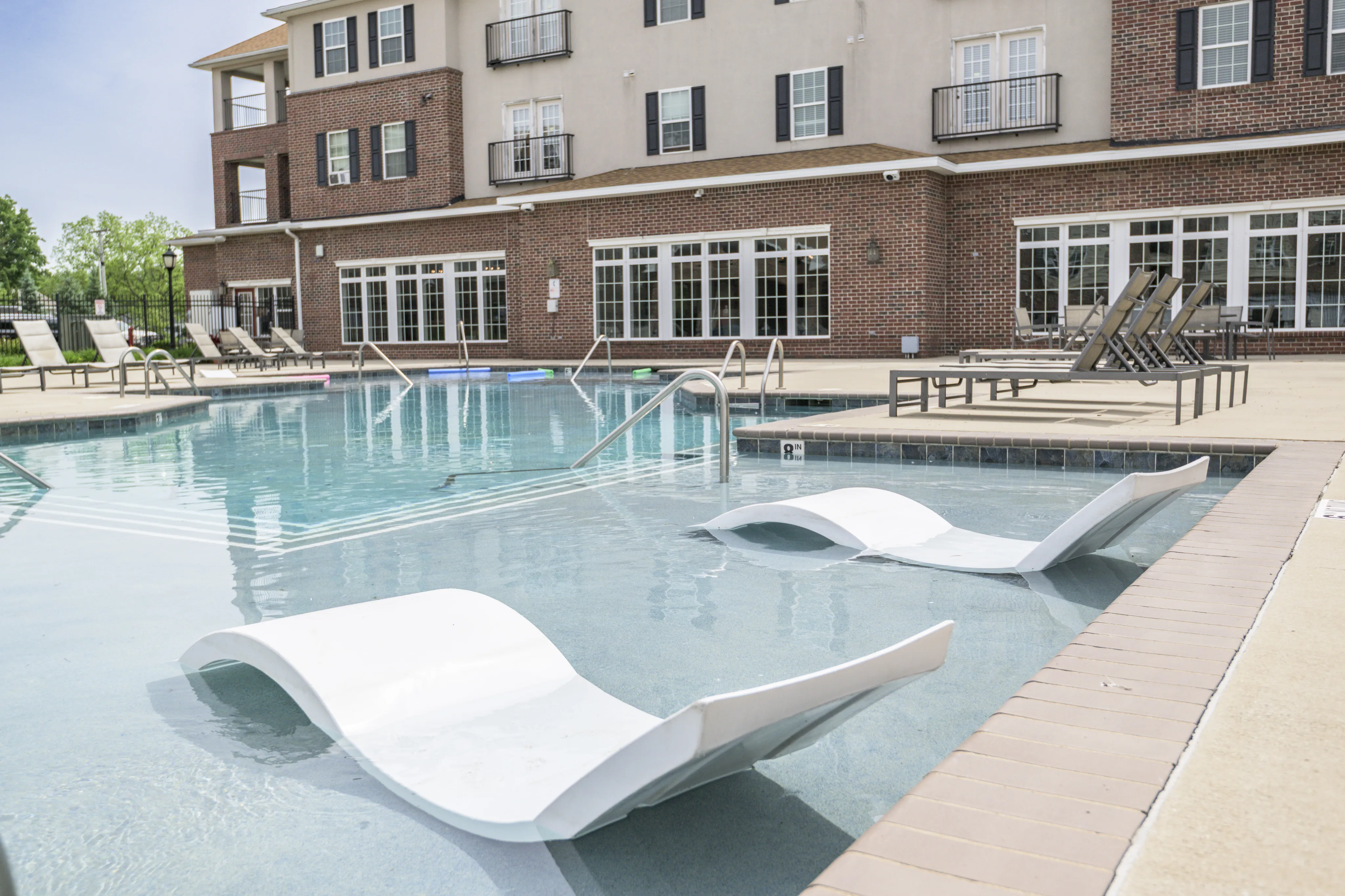 Inviting outdoor pool area with modern poolside loungers and brick apartment backdrop.
