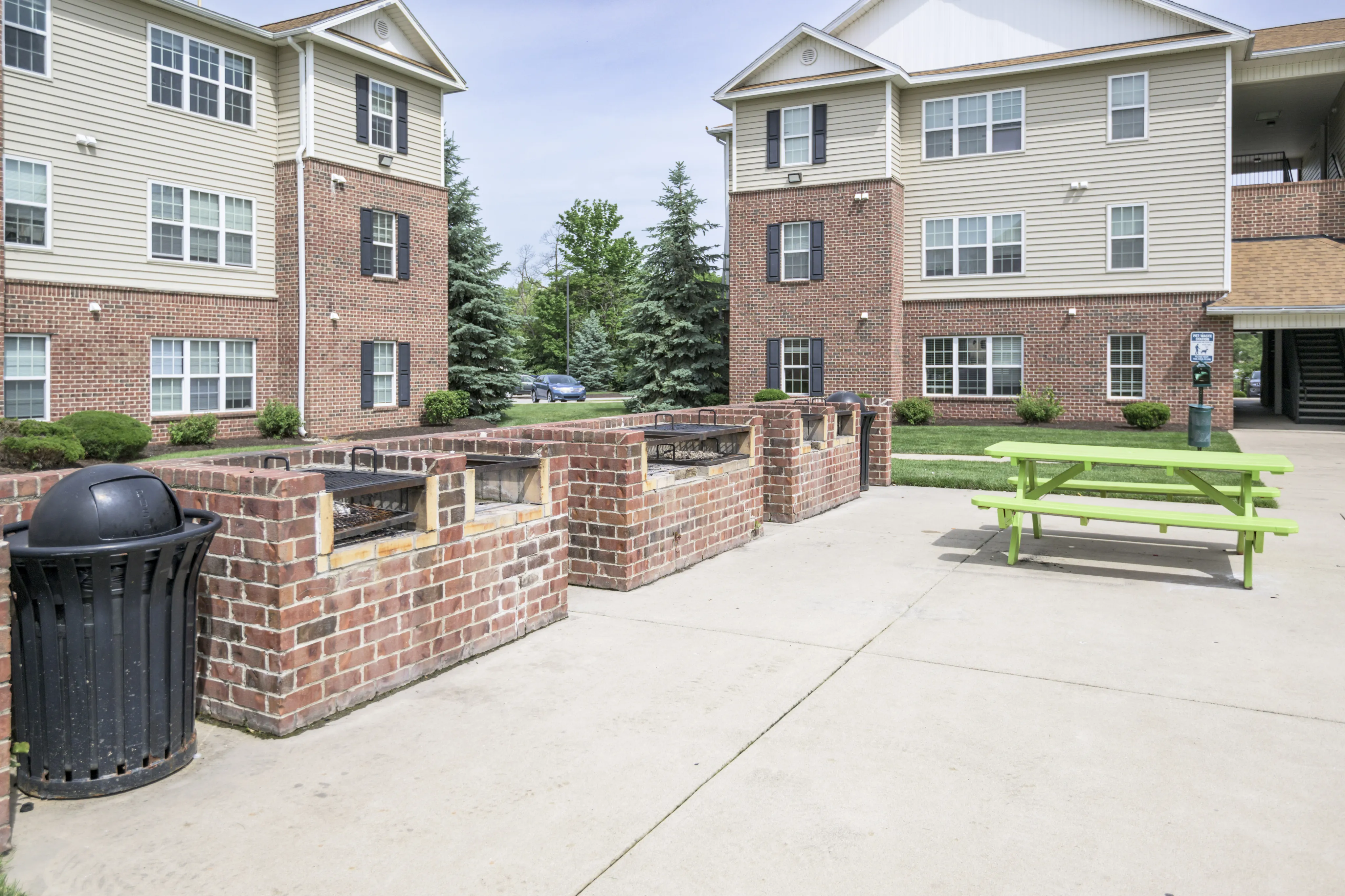 Charming apartment exterior with brick facade, lush landscaping, and inviting picnic area with outdoor grills.
