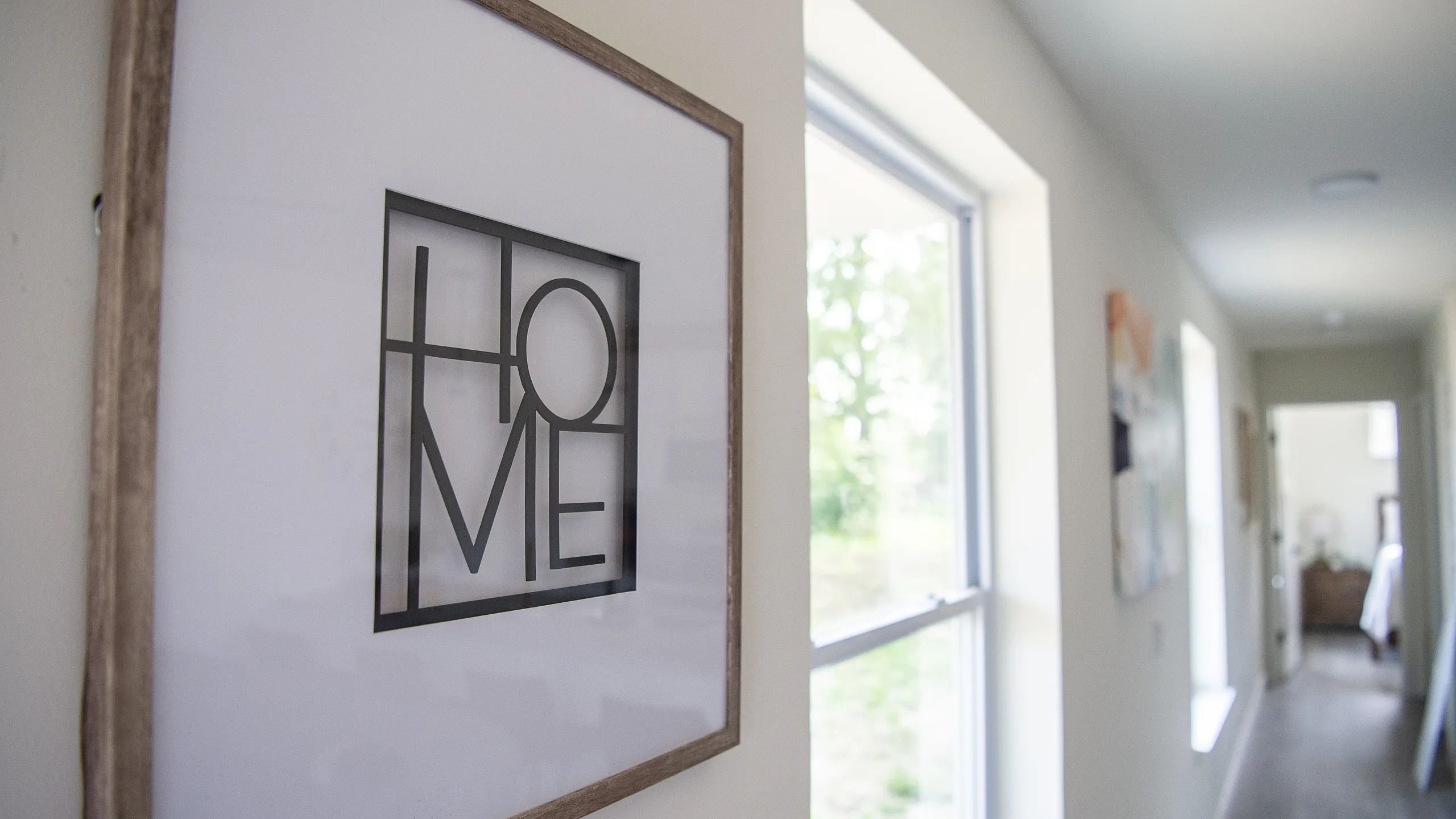 Inviting hallway with natural light and stylish 'Home' art print, leading to a cozy room, enhancing the welcoming atmosphere.