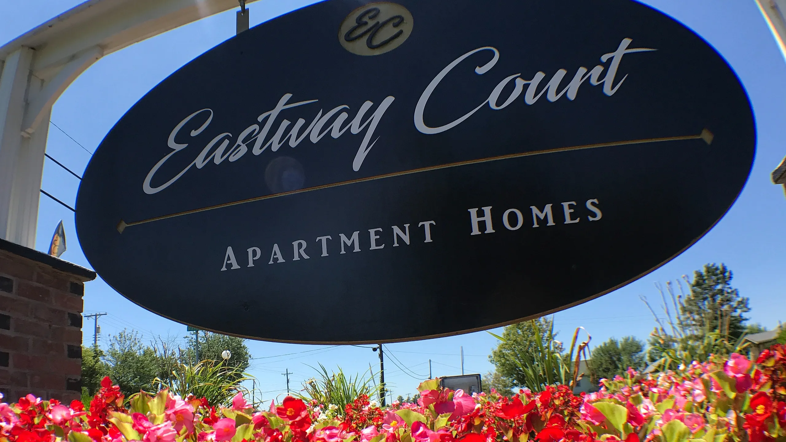 Inviting entrance sign of Eastway Court Apartment Homes surrounded by vibrant blooming flowers under a clear blue sky.