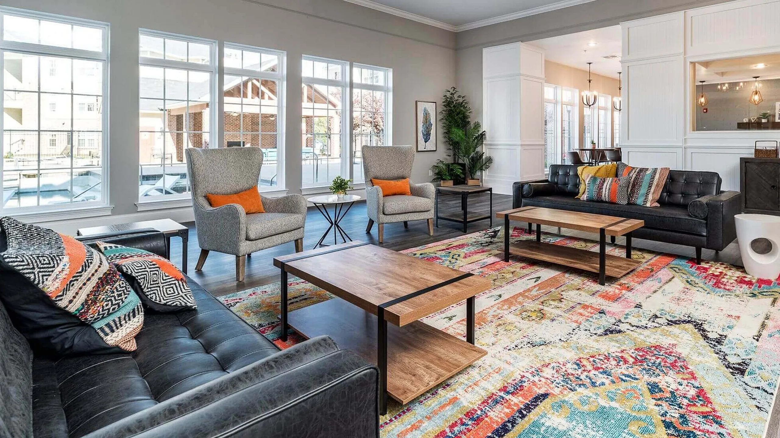 Inviting living room with cozy seating, vibrant rug, large windows, and stylish lighting.