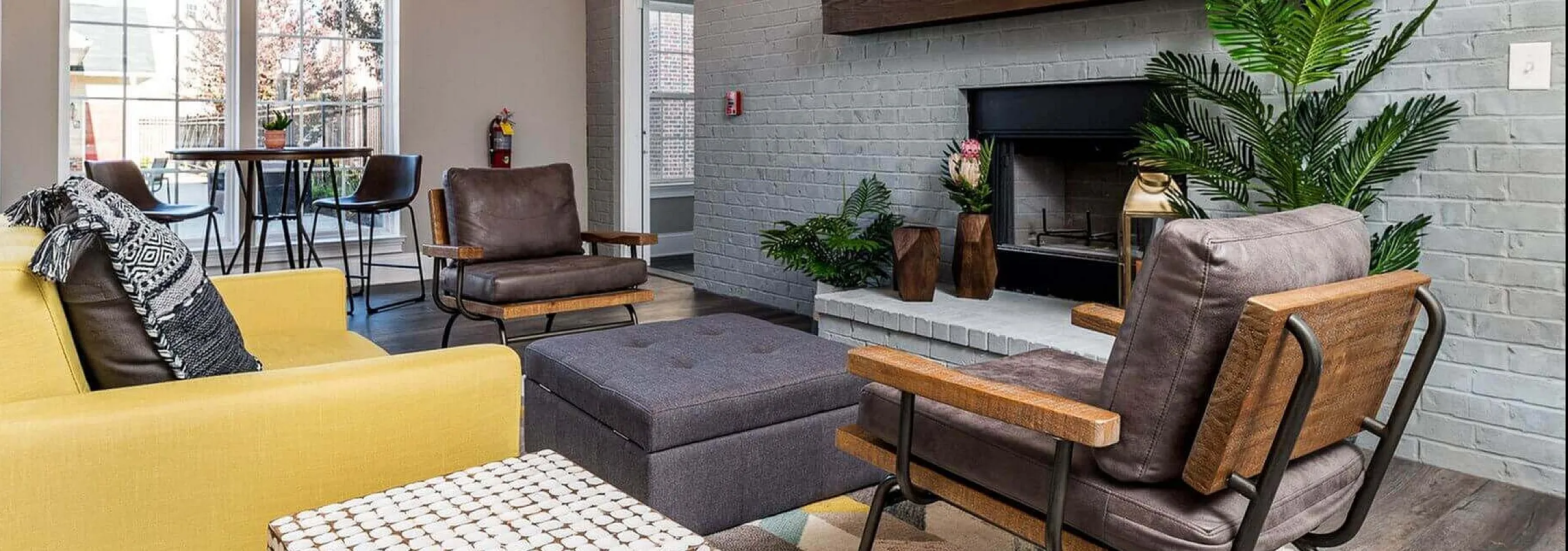 Inviting living room featuring modern decor with vibrant yellow sofa, sleek armchairs, and rustic fireplace. Natural light floods through large windows, enhancing the cozy atmosphere.