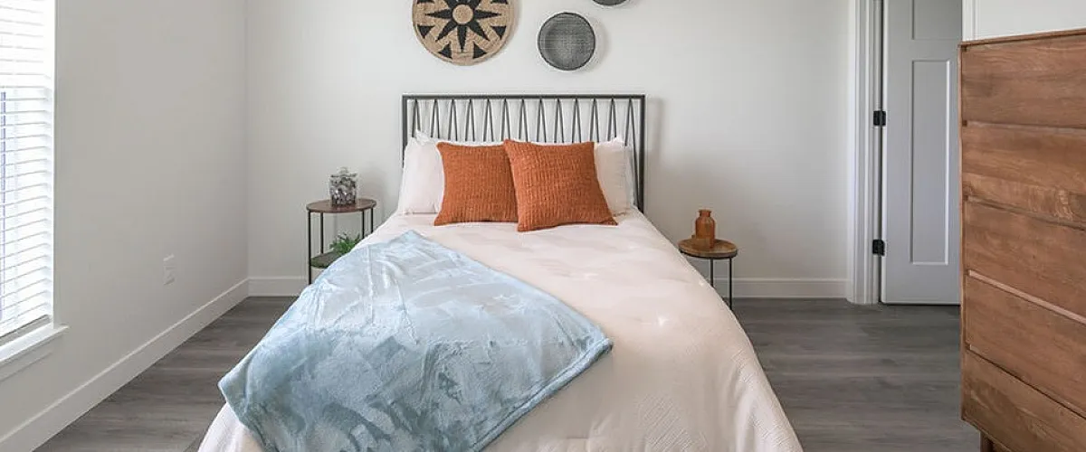 Bright and inviting bedroom with stylish decor, featuring a comfortable bed with cozy blankets and pillows, modern wall art, and a sleek wooden dresser on elegant hardwood flooring.