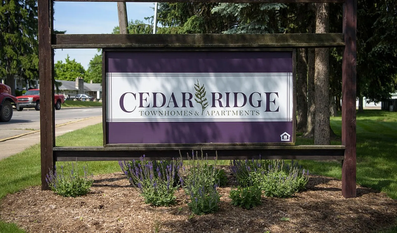 Inviting entrance sign of Cedar Ridge Townhomes & Apartments surrounded by lush greenery and vibrant landscaping.