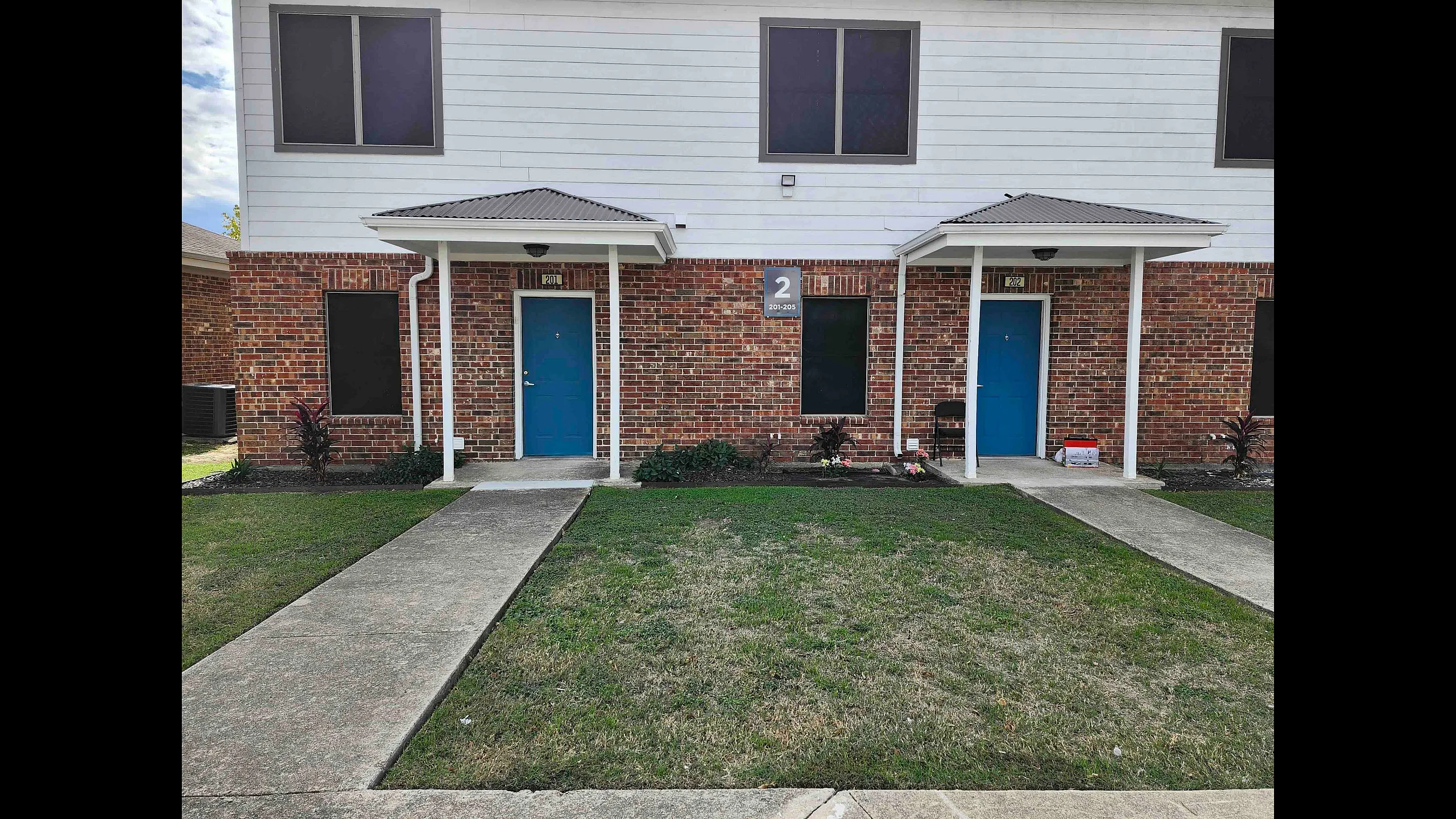 Inviting entrance of a brick apartment building with blue doors and well-maintained landscape.