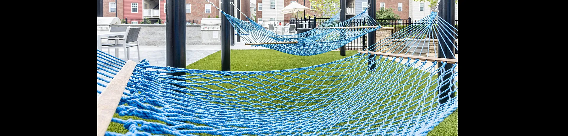 Inviting outdoor area featuring blue hammocks set on green artificial turf with apartment buildings in the background.