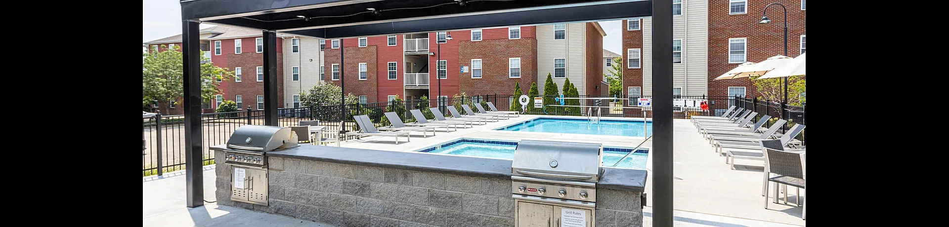 Outdoor area with a swimming pool, lounge chairs, and a BBQ grill under a shaded structure.