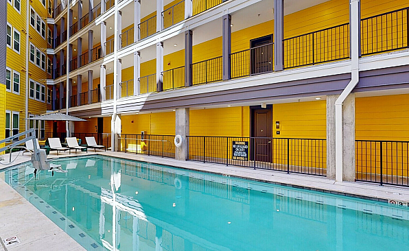Vibrant apartment complex featuring a sparkling outdoor pool with modern lounge chairs, framed by bright yellow walls and sleek balconies.