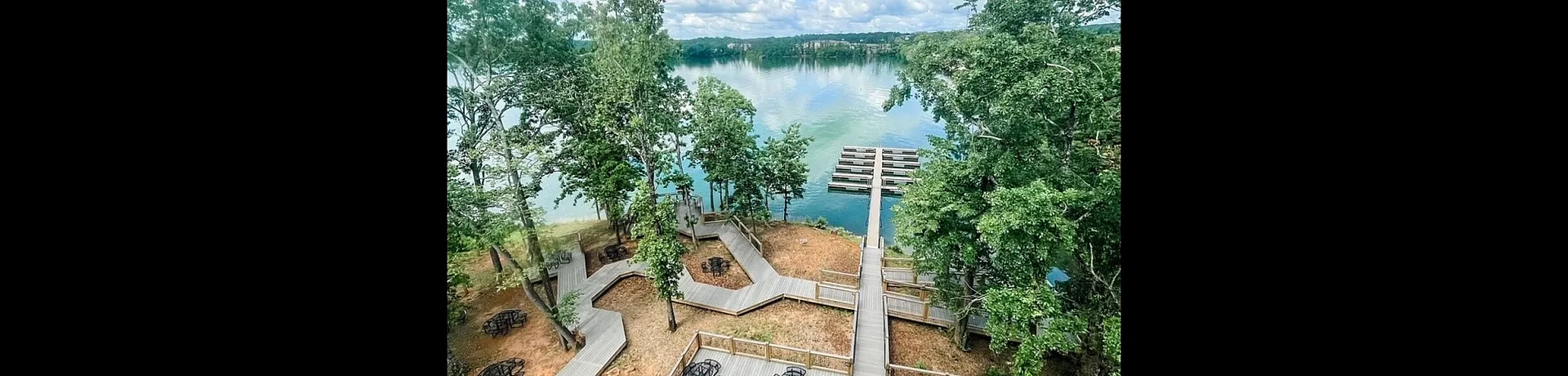 Stunning lakefront view with a beautifully designed wooden pathway and seating areas surrounded by lush greenery, offering a peaceful retreat and serene water views.