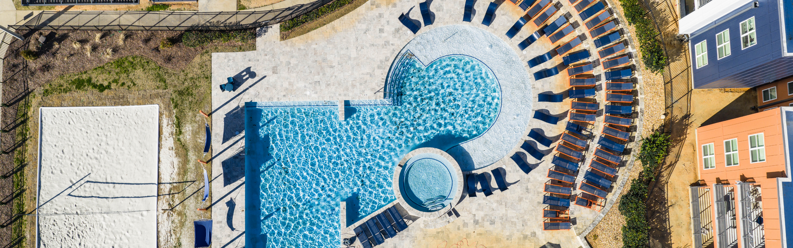 Luxurious aerial view of a sparkling swimming pool surrounded by stylish lounge chairs and vibrant buildings, offering a perfect relaxation spot.