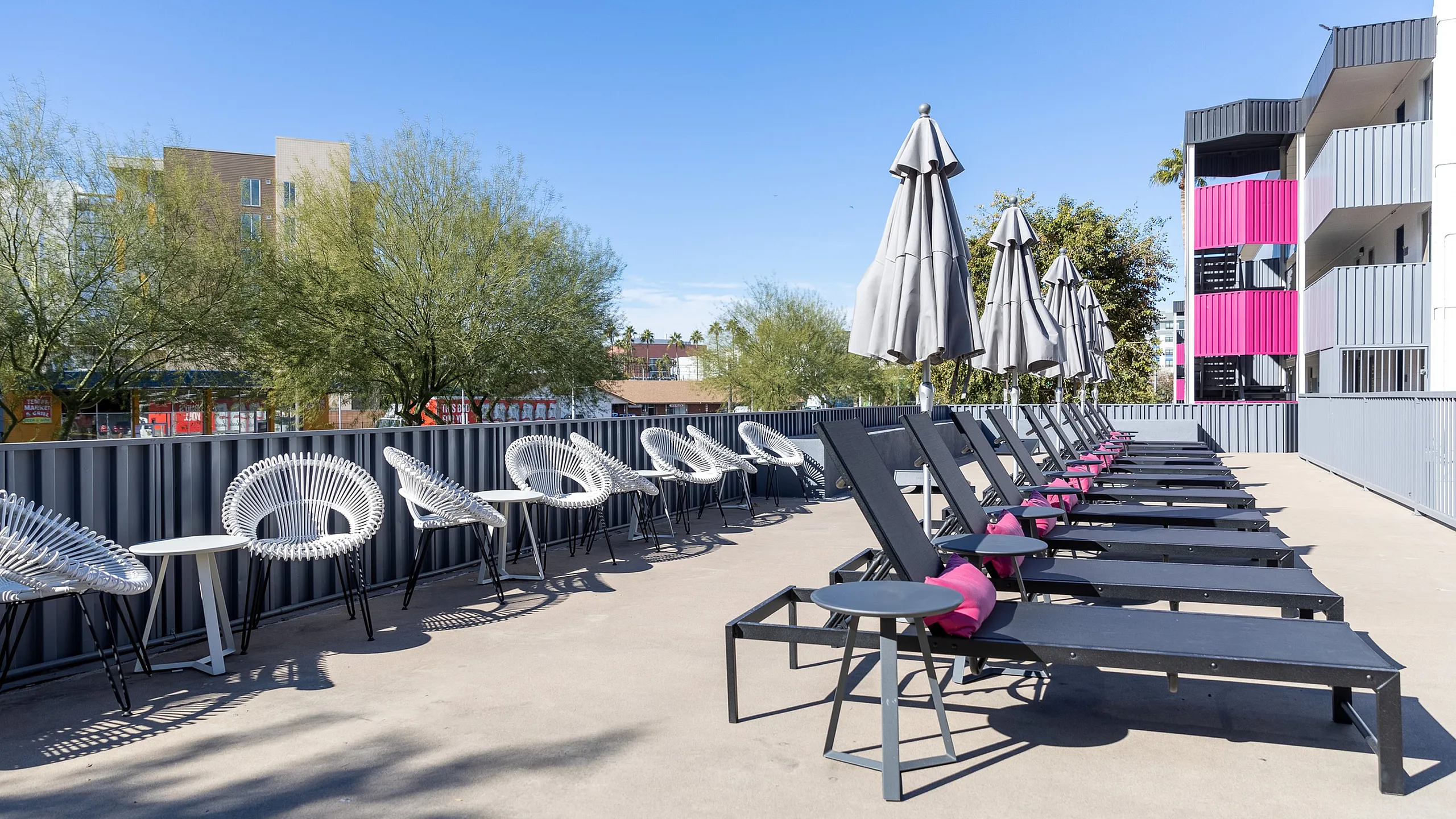 Modern outdoor lounge area featuring stylish sun loungers, chic round chairs, and sleek umbrellas against a vibrant urban backdrop.