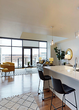 Modern open-concept apartment featuring a sleek kitchen with wood cabinetry and a bright living area with large windows overlooking the city.