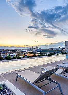 Breathtaking rooftop pool with sleek lounge chairs overlooking a vibrant cityscape and stunning mountain views at sunset.