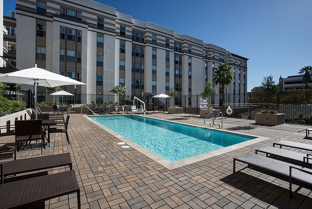 Modern apartment complex with a stunning outdoor pool, surrounded by elegant seating and palm trees under a clear blue sky.