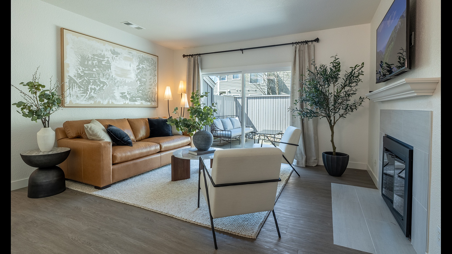 Inviting living room with modern decor, featuring a cozy leather sofa, elegant armchairs, a contemporary fireplace, and a serene view through large windows.