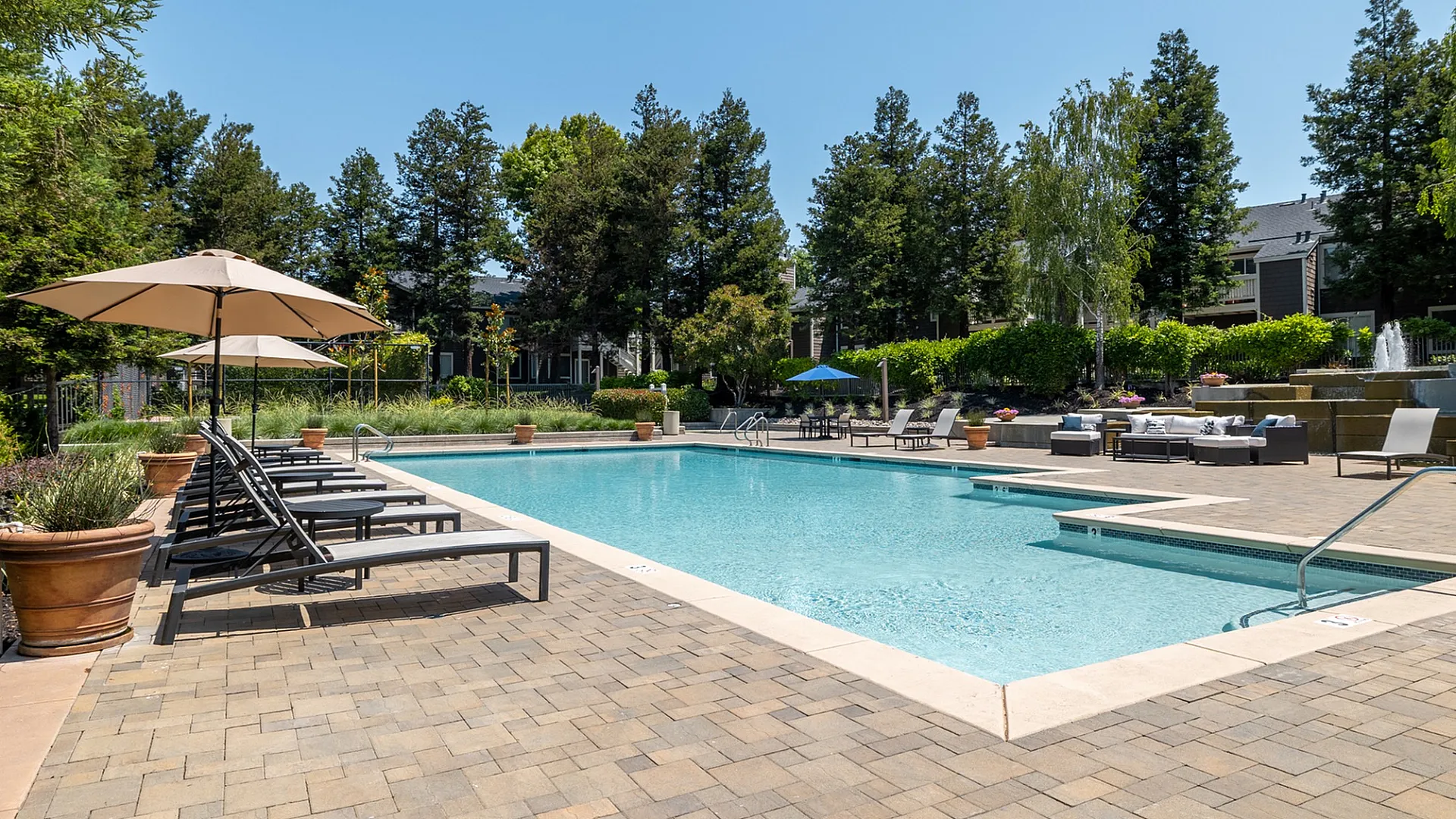 Luxurious outdoor pool area surrounded by lush greenery, featuring comfortable lounge chairs and elegant umbrellas, perfect for relaxation and sunbathing.