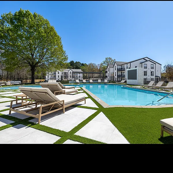 Luxurious apartment complex featuring a stunning outdoor pool surrounded by modern lounge chairs and lush greenery under a clear blue sky.