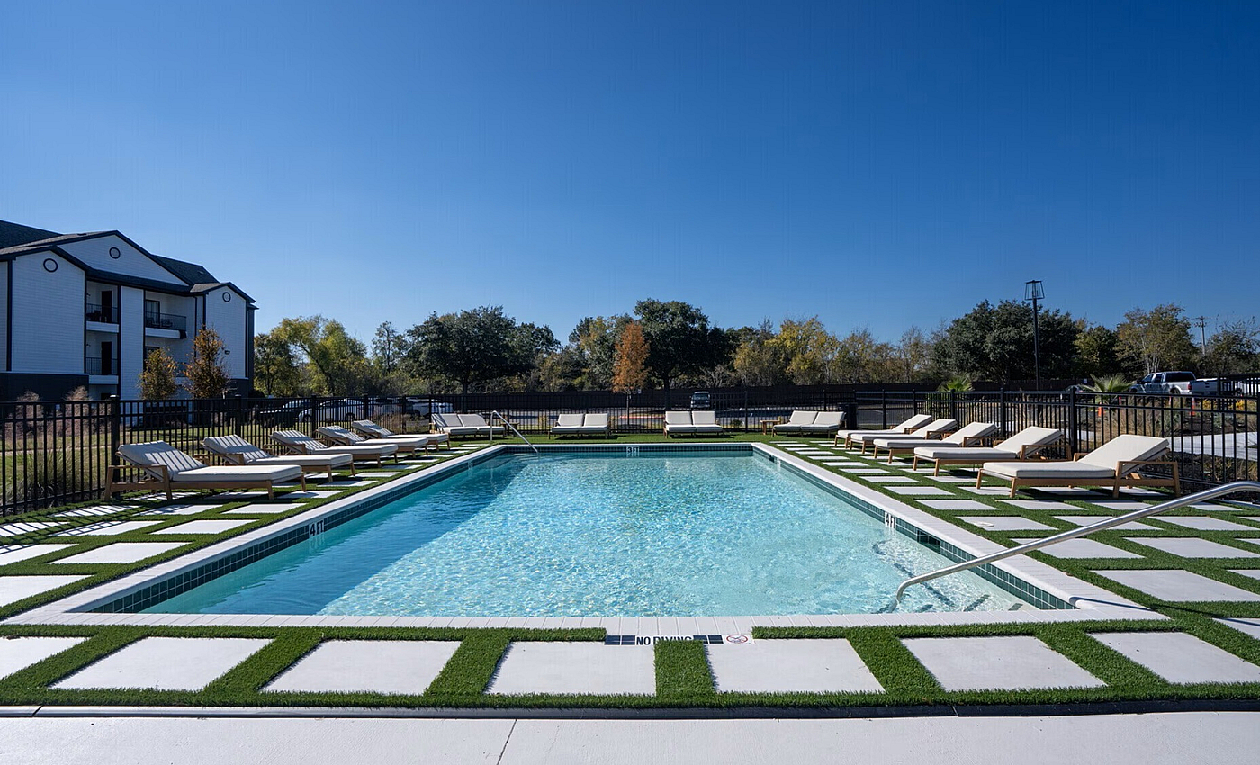 Inviting apartment complex pool surrounded by stylish lounge chairs and vibrant greenery, perfect for a relaxing retreat.