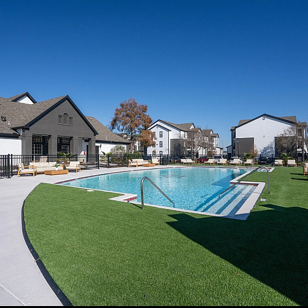 Inviting apartment community with a sparkling swimming pool, cozy lounge chairs, and well-maintained landscaping under a clear blue sky.