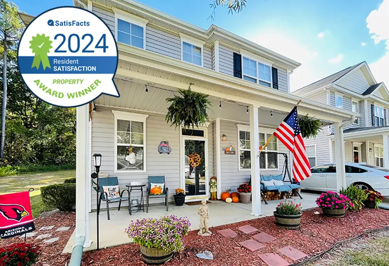 Inviting two-story home with a welcoming front porch adorned with plants and flags, celebrating 2024 satisfaction award.