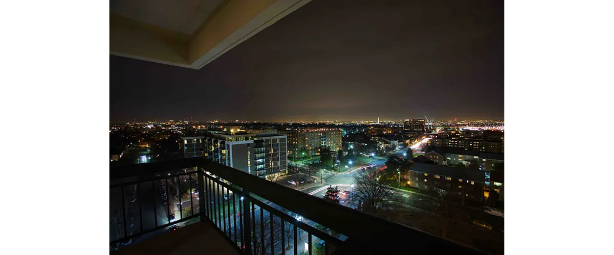 Breathtaking cityscape view from an apartment balcony, showcasing vibrant city lights and a lively urban skyline at night.