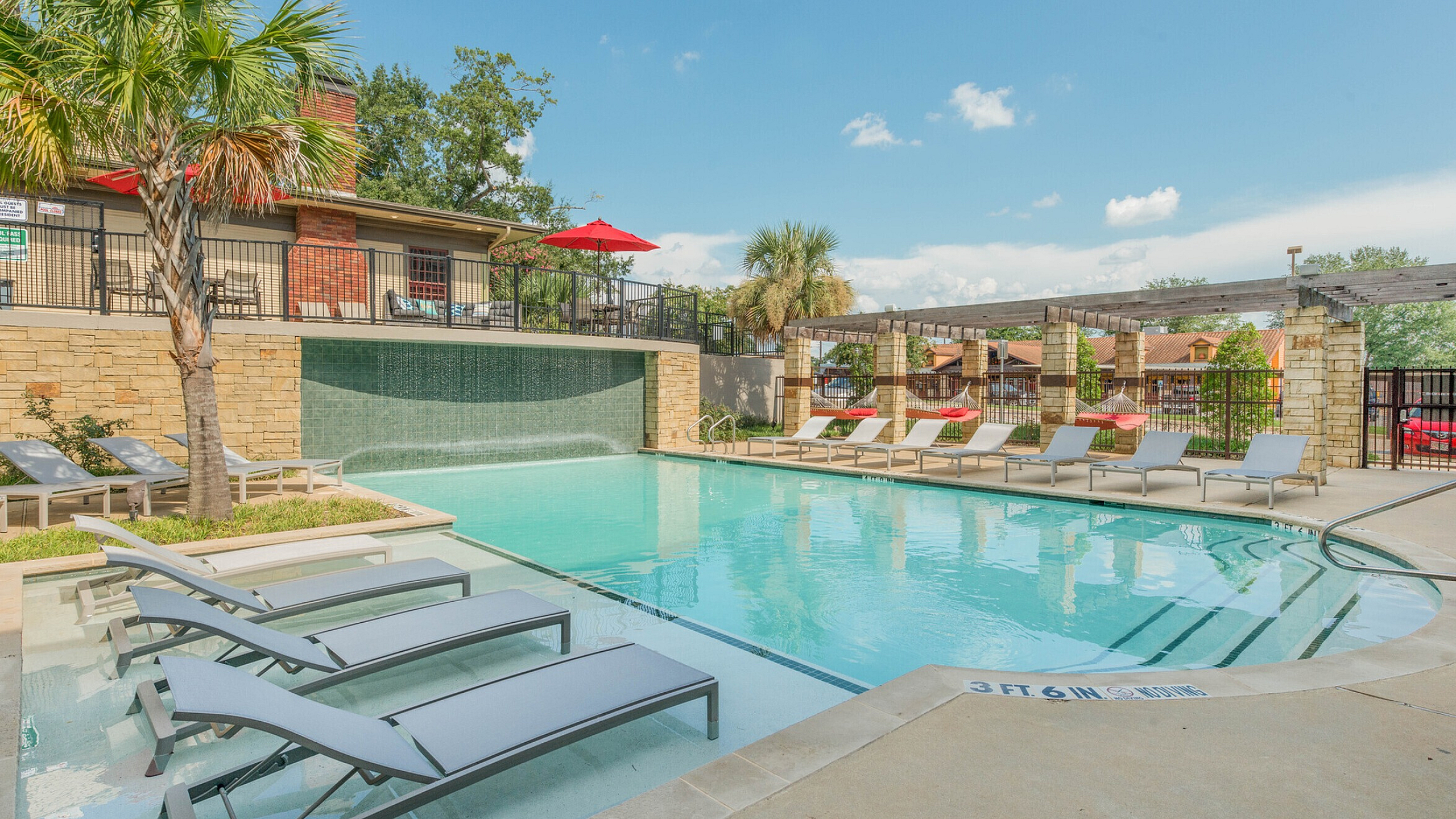 Luxurious pool area featuring sun loungers, a cascading waterfall, and vibrant red umbrellas, perfect for relaxation.