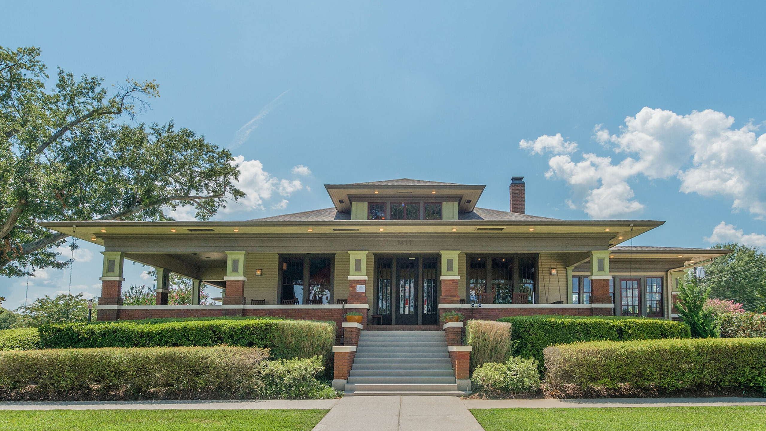 Charming Craftsman-style home with a welcoming front porch, manicured lawn, and classic architectural detailing under a bright blue sky.