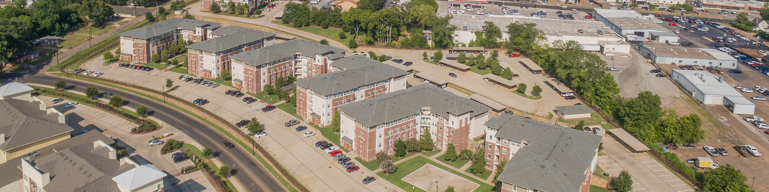 Aerial view of a vibrant apartment neighborhood surrounded by lush greenery, showcasing modern buildings and ample parking spaces.
