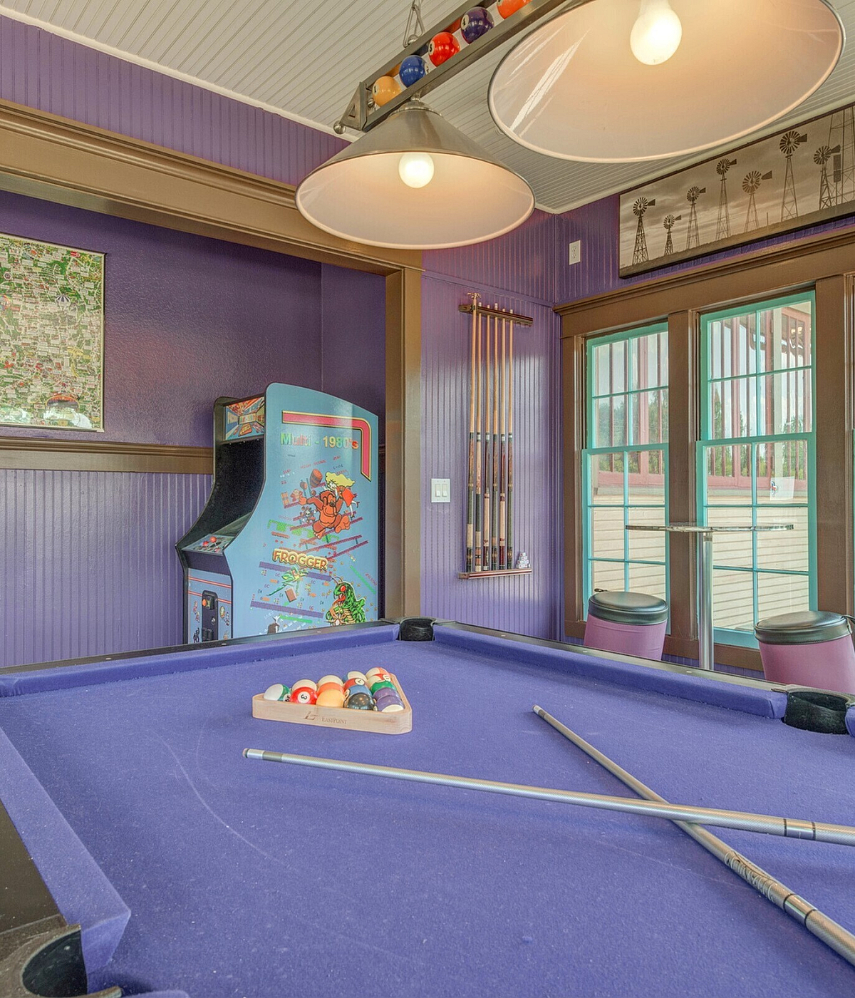 Vibrant game room with a bold purple pool table, classic arcade machine, and large windows inviting natural light.