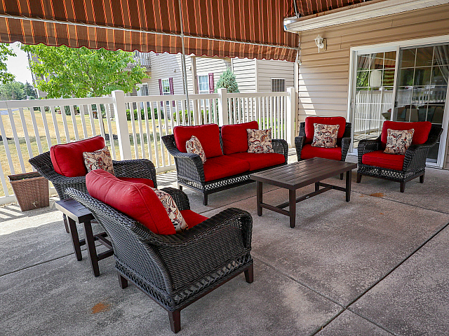 Charming outdoor patio with stylish wicker furniture featuring vibrant red cushions, under a striped canopy.