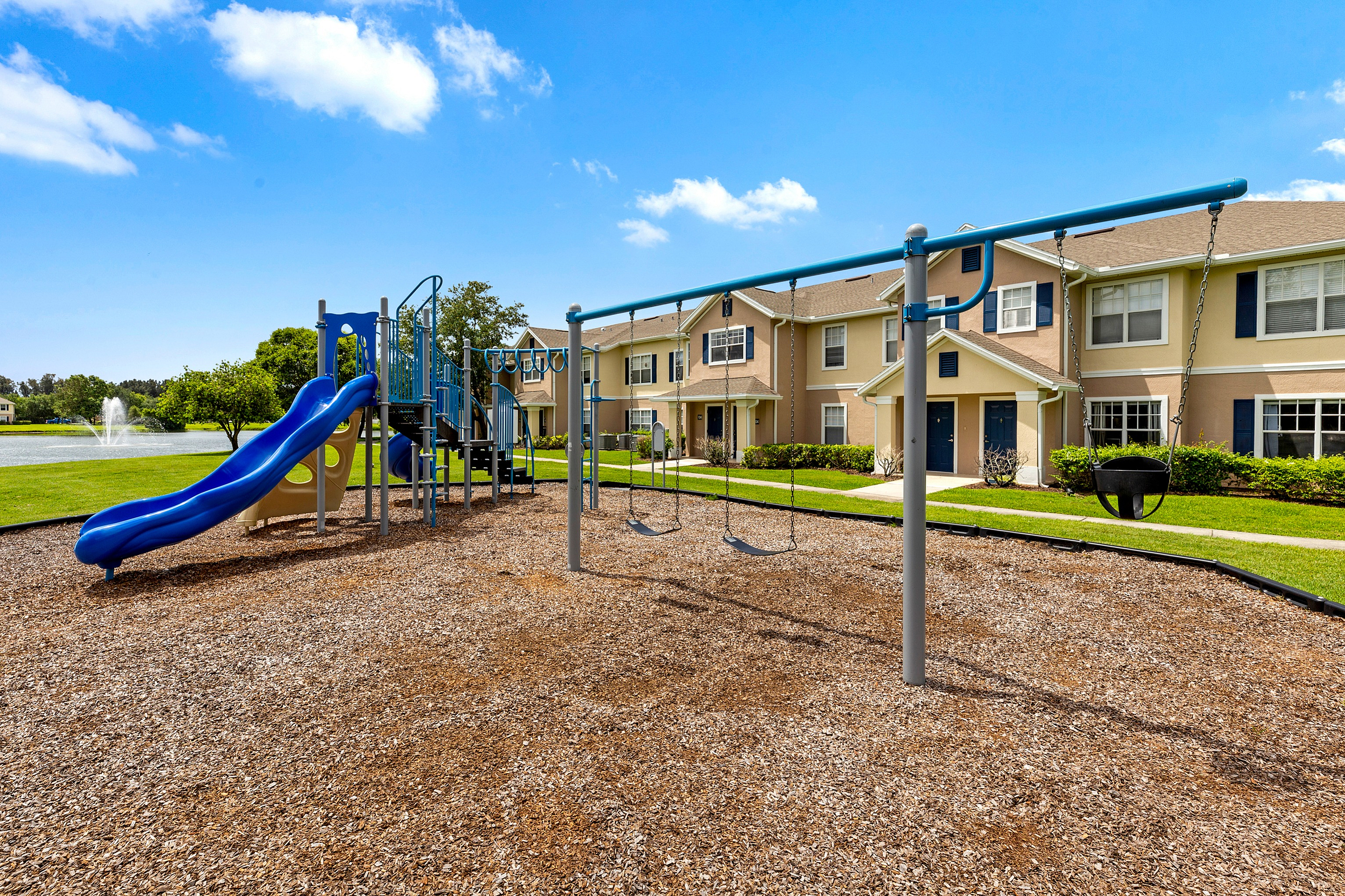 Charming residential community with modern playground, lush greenery, and serene pond backdrop.