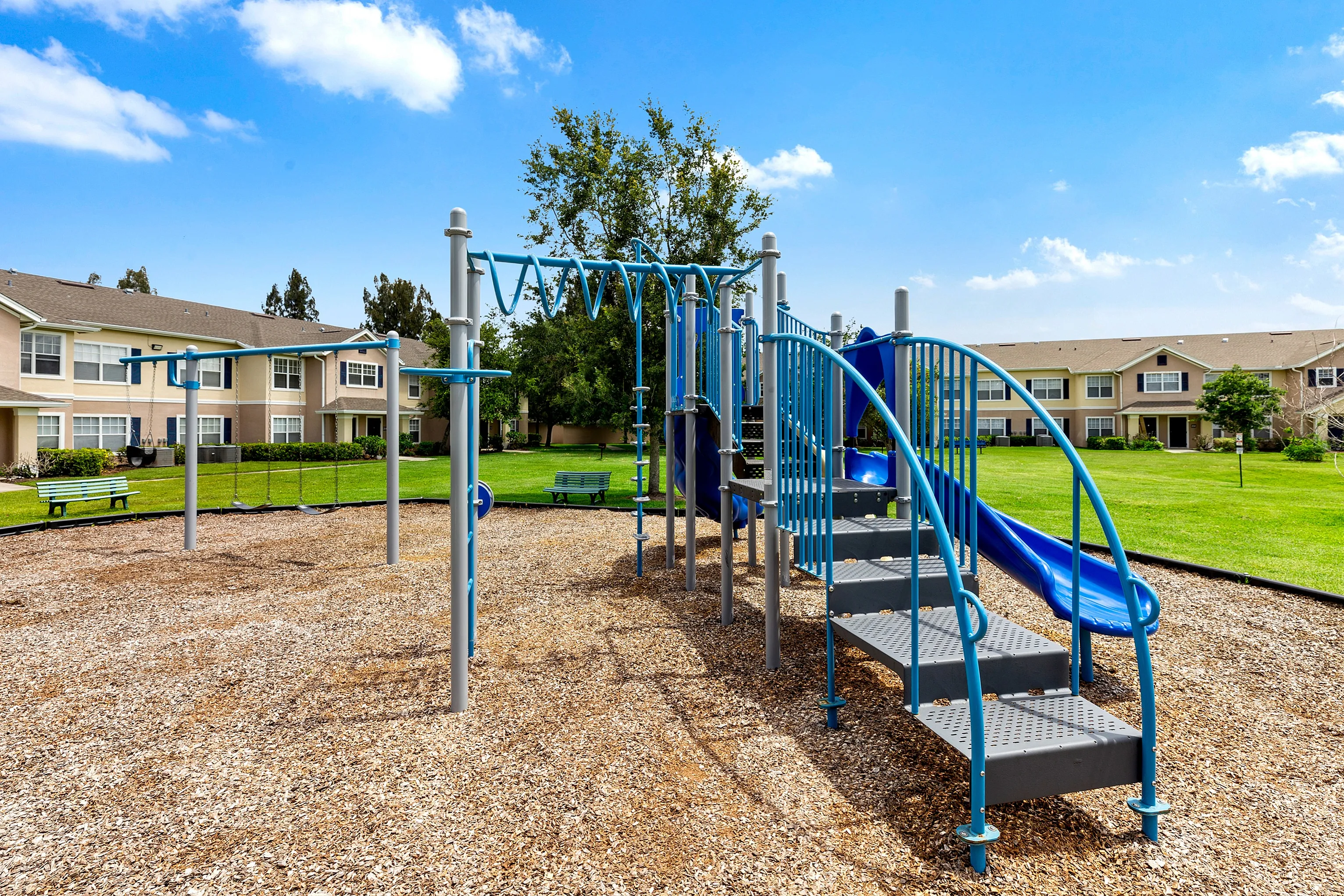 Charming community playground with modern equipment, surrounded by lush green lawns and inviting apartment homes.