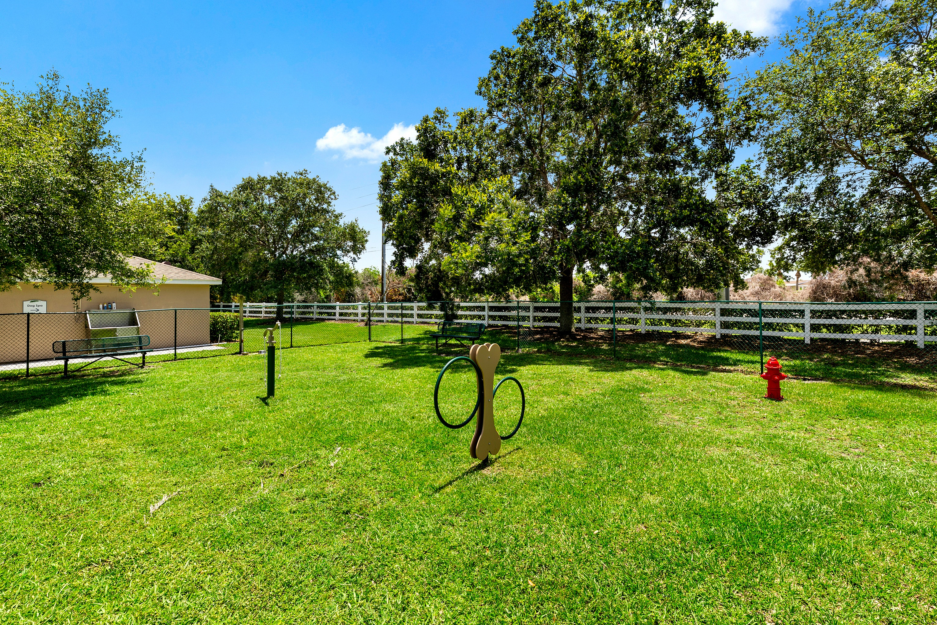 Charming fenced dog park with lush green grass, trees, and playful structures, perfect for pet-friendly enjoyment.