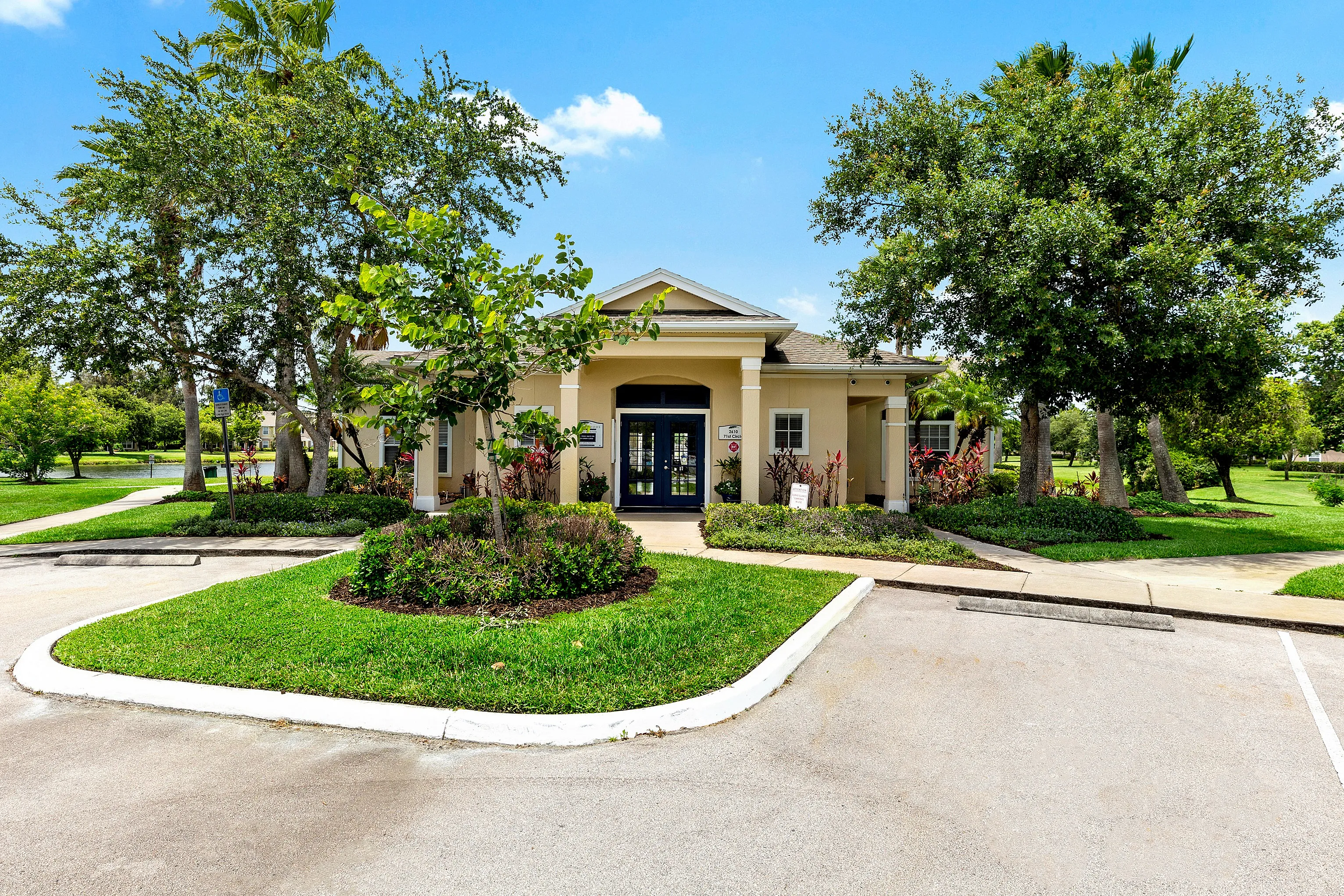 Charming community clubhouse surrounded by lush greenery and vibrant landscaping, set against a clear blue sky.